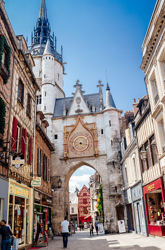 Auxerre, France - July 30, 2014: Tourists and locals shopping beside the Clock Tower in the Old Town district of Auxerre in the Burgundy region of France. The tower dates from 1483 with the clock added in the 17th century. Its hands show the time, and the phase of the Moon.