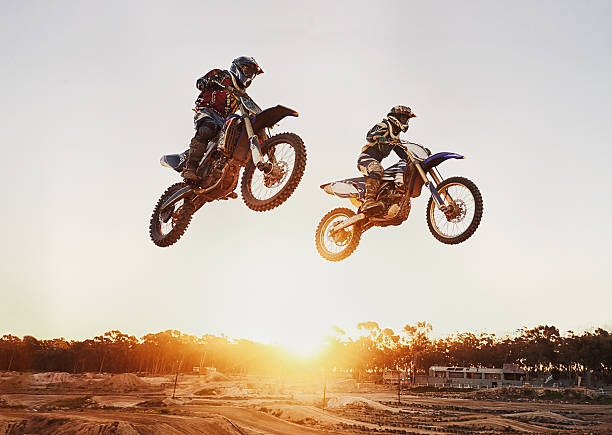Jumping over the sunset A shot of two motocross riders in midair during a race motorcycle racing stock pictures, royalty-free photos & images