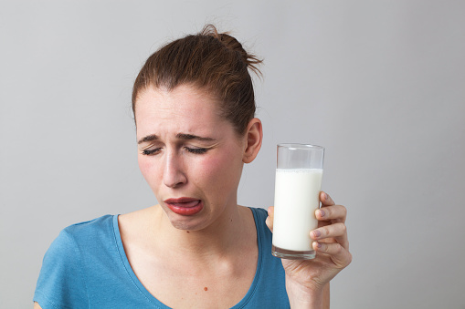 young woman with nausea not willing to drink a glass of smelly milk or disgusting white beverage