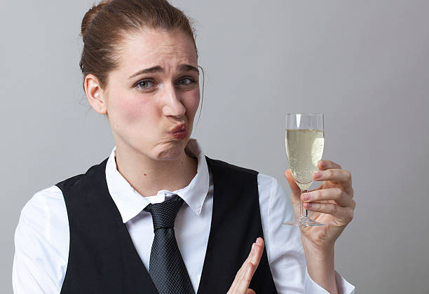Dubious 20s girl resisting in drinking more Champagne at party Embarrassed young woman wearing uniform of wine waitress refusing glass of white bubbly wine awful taste stock pictures, royalty-free photos & images