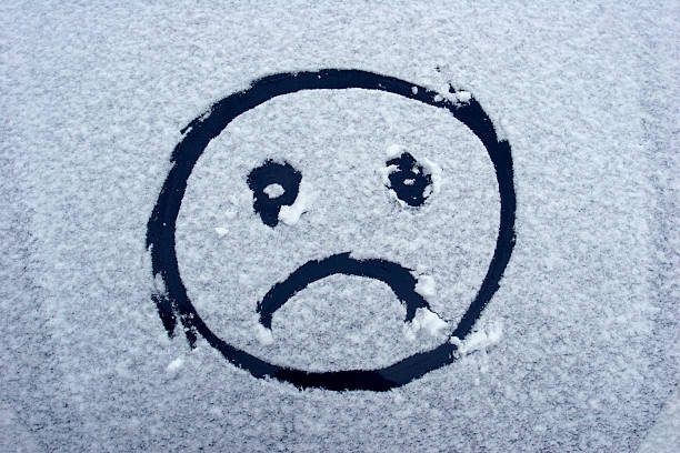 An unhappy smiley face drawn on a snow covered windshield.