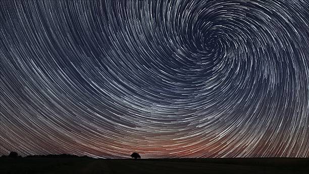 istock Beautiful Spiral Star Trails over filed with lonely tree. 486478828