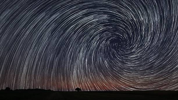 istock Beautiful Spiral Star Trails over filed with lonely tree. 486478830