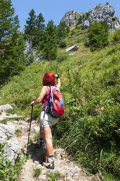 Pretty middle aged woman hiker pointing the direction on the mountain peak with her walking pole, selective focus on lady