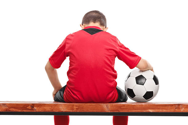 traurige kleine junge in rote trikot, auf einer bank sitzend - soccer child indoors little boys stock-fotos und bilder