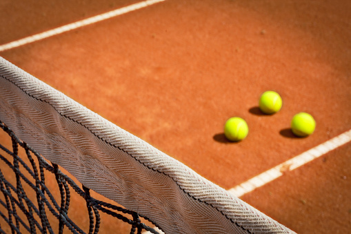 Tennis net and three balls on the clay court in background