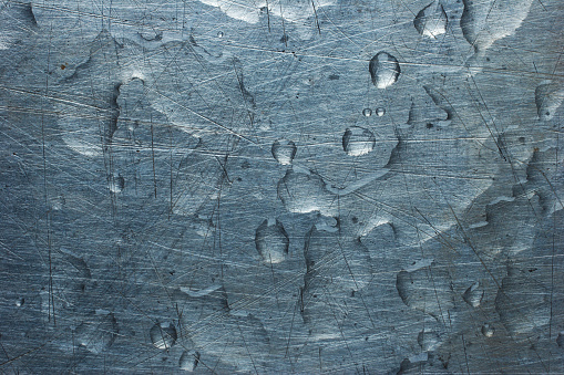 A silver-blue metal scratched and textured with water droplets on it.