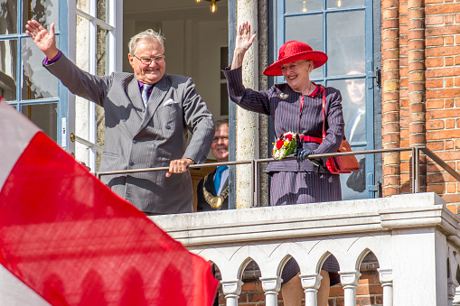 Vejle, Denmark - September 2, 2015: The Queen Margrethe of Denmark is visiting the city of Vejle together with her husbond Prince Henrik. They are waving from the balcony of the Vejle Town Hall to a large crowd of people. The visit is one of many visiting danish coastal towns. In the foreground the red and white national flag called \