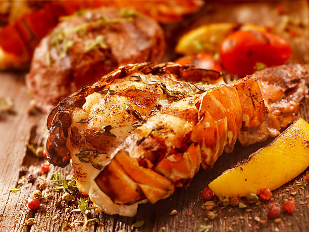 BBQ Grilled Lobster Tail and Steak Fillet BBQ Grilled Lobster Tail and Steak Fillet with Fresh Herbs, Grilled Lemon and Tomatoes -Photographed on Hasselblad H3D2-39mb Camera tail fin stock pictures, royalty-free photos & images