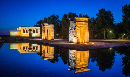 The ancient Egyptian stone pylons of the Temple of Debod, spotlit against the deep blue dusk skies in the Parque del Oeste in the heart of Madrid, Spain's vibrant capital city. ProPhoto RGB profile for maximum color fidelity and gamut.