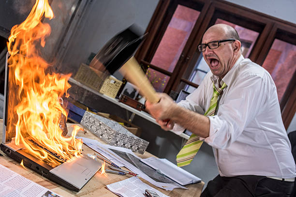 зрелый взрослый бизнесмен smashing ноутбук на огонь с молотом - fury стоковые фото и изображения