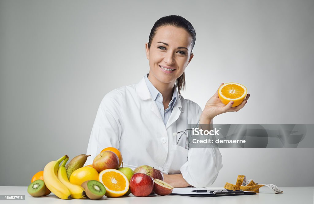 Dietician holding an orange Smiling dietician sitting at desk and holding an orange Nutritionist Stock Photo