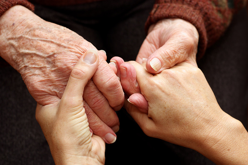 The hands of a young woman takes those of an older person as a sign of support and help