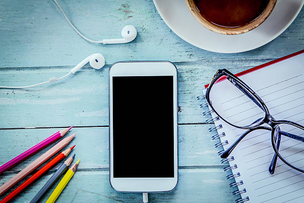 Smartphone,cellphone,notebook,pencil color,glasses and coffee on wooden table in blue vintage filter