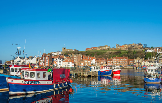 View of the harbour at Whitby with fishing boats in the foreground and the famous Whitby Abbey on the hill.