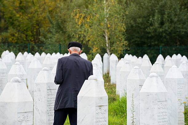 Muslim man at Srebrenica cemetery Srebrenica, Bosnia and Herzegovina - October 11, 2013: A Muslim man offers a prayer while visiting the graves of friends and family at the Srebrenica-Potočari Genocide Memorial and Cemetery, where the remains of more than 6000 Bosnian Muslims killed by Bosnian Serbs in July 1995 have been laid to rest. ethnic cleansing stock pictures, royalty-free photos & images