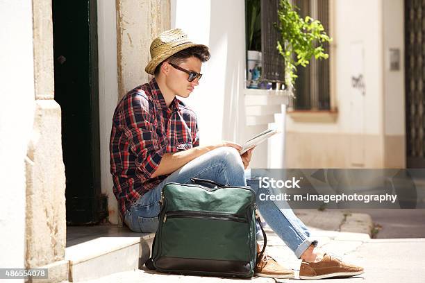 Traveling Man Sitting On Sidewalk Reading Map Stock Photo - Download Image Now - 20-29 Years, 2015, Activity