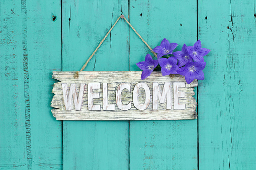 Rustic welcome sign with purple balloon flowers hanging on antique teal blue wooden background