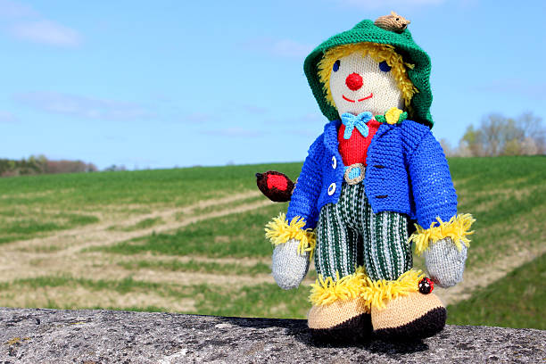 istock Image of friendly knitted scarecrow toy against field background 486569327