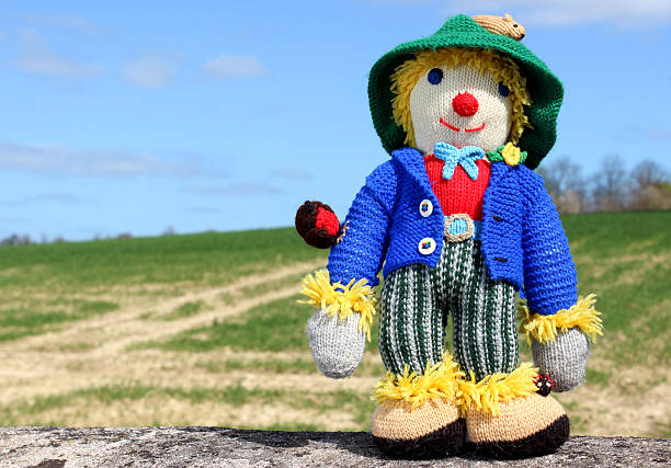istock Image of friendly knitted scarecrow toy against field background 486569333