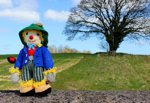 istock Image of friendly knitted scarecrow toy against field background 486569351