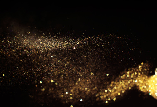Golden glitter waving on black background. Studio shot using high speed technique, selective focus.
