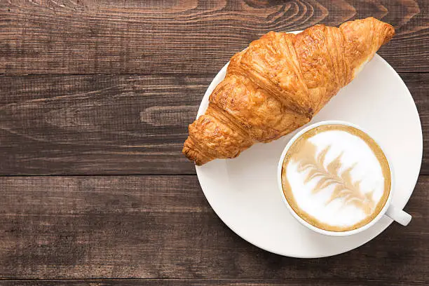 Coffee cup and fresh baked croissants on wooden background. Top View.
