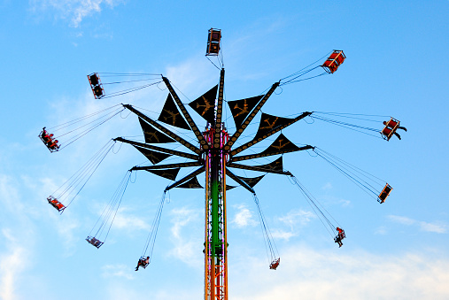 People on high rise swing at county fair.  They are seen against the sky.  You can hear them screaming from either fun or fear.