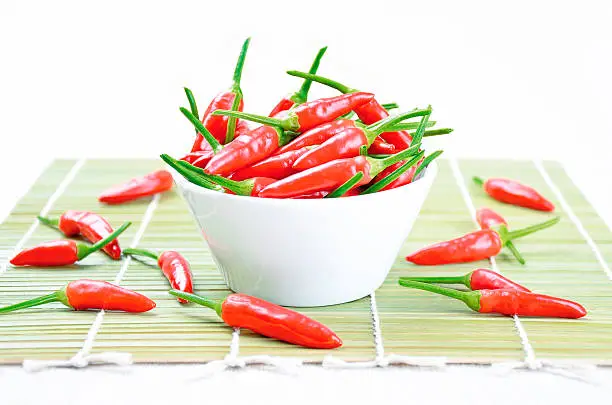 Red hot chili peppers in a white bowl on a green bamboo mat