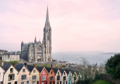Cork, Ireland - March 24, 2012: St. Colman's Cathedral situated in Cobh, Cork photographed at sunset with a row of multi-colored terraced houses in the foreground.