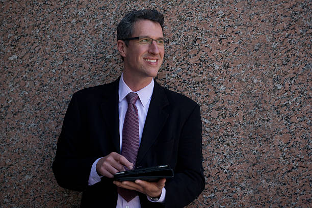 smiling mature businessman outside an office building using tablet - foto’s van leiderschap stockfoto's en -beelden