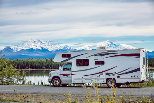 An RV parked in front of a lake in Alaska near Wrangell St. Elias National Park. In the background are Mt. Sanford and Mt. Drum.