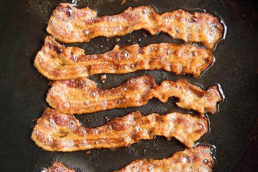 Bacon strips being cooked in frying pan. Close up