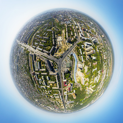 Aerial city view with crossroads and roads, houses, buildings, parks and parking lots, bridges. Copter shot. Little planet sphere mode.