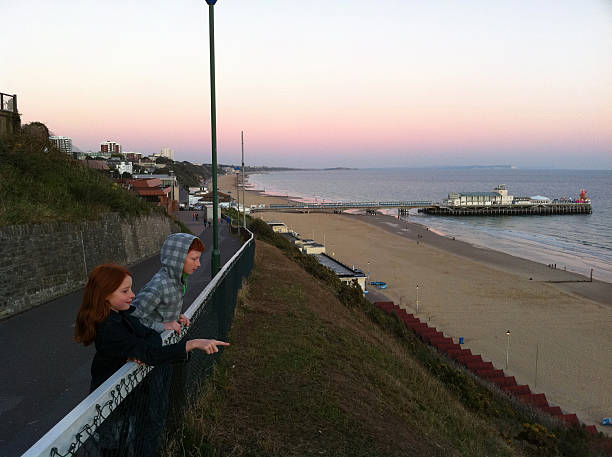 Image showing a young boy and girl (brother and sister) on a cliff top walk at Bournemouth, Dorset, England, UK, looking at the beach, sea and distant pier.  This photo was taken just as the sun was beginning to set.