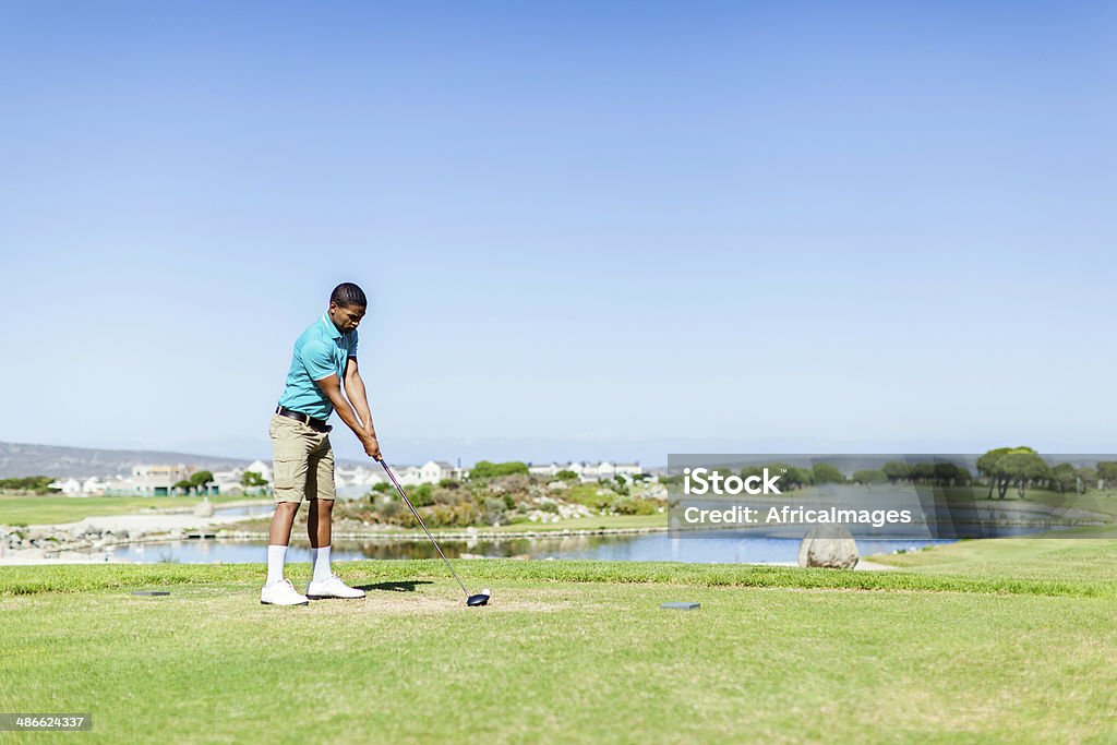 African golfer looking at the ball, ready to hit it. African golfer ready to hit the golf ball at the starting point. Langebaan, Western Cape, South Africa 20-24 Years Stock Photo