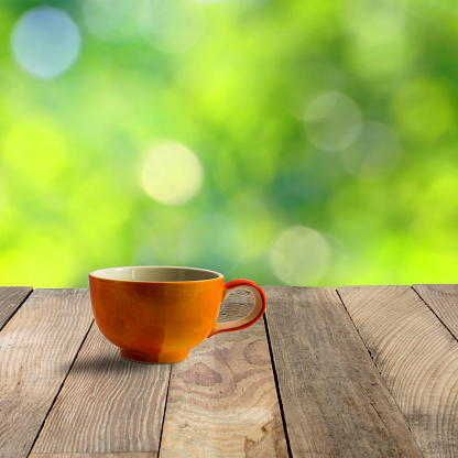 Orange cup on wood table and green blurred backgrounds.