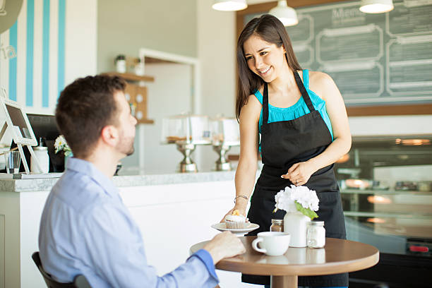 Gorgeous young Latin waitress bringing a cupcake and some coffee to a customer in a cafe