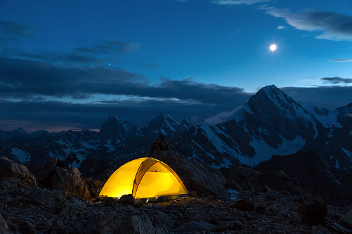 Illuminated Camping Yellow Tent Night High Altitude Alpine Landscape Shining Moon in Dark Blue Sky cooler tone