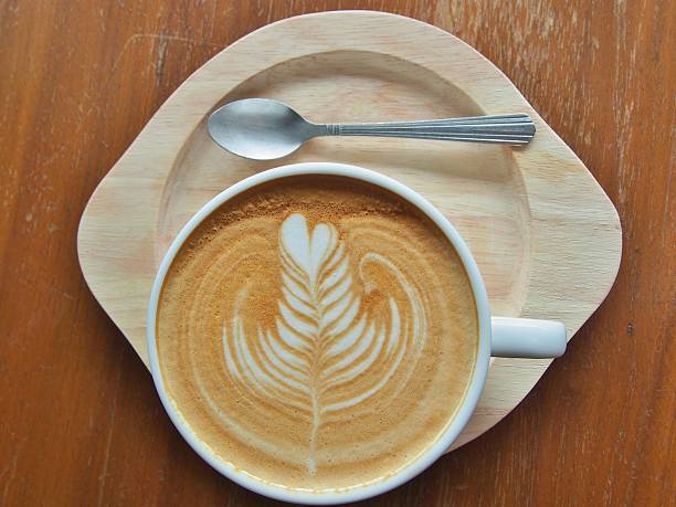 coffee with latte art and steel spoon on wooden saucer