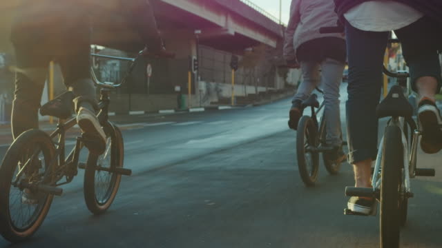 A group of BMX biker is driving through the streets of a city. They cruising around and making some tricks.