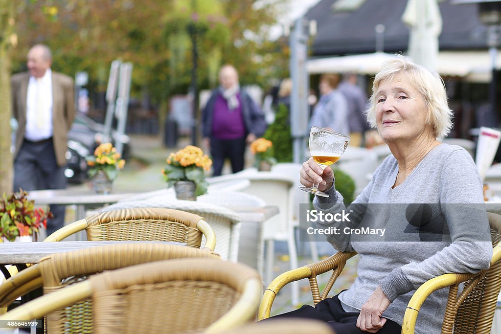 Happy active senior woman relaxing in outdoors cafe Happy joyful senior woman sitting outdoors in cafe drinking cold fresh beer City Stock Photo