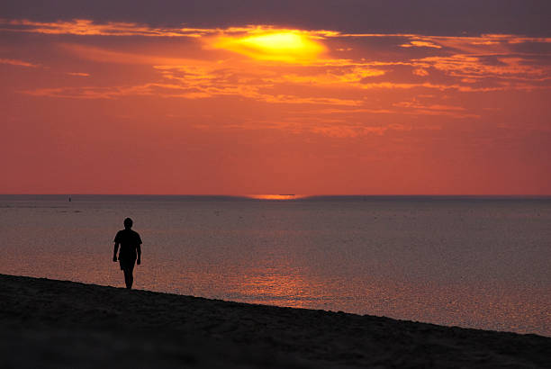 istock Man walks across empty beach watching summer sunset at sea 486646836
