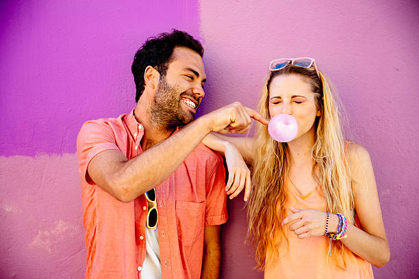 Playful man popping chewing gum bubble girl Happy playful young couple against pink background bubble gum photos stock pictures, royalty-free photos & images
