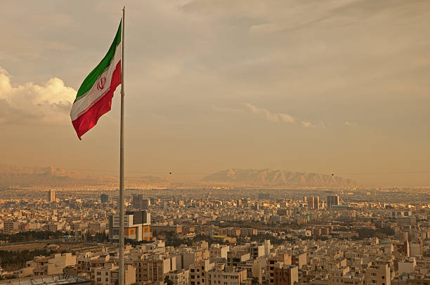 bandiera dell'iran nel vento sopra la skyline di teheran - teheran foto e immagini stock