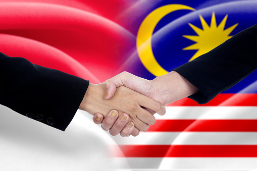 Two entrepreneurs shaking hands after good deal in front of the indonesian and malaysian flags