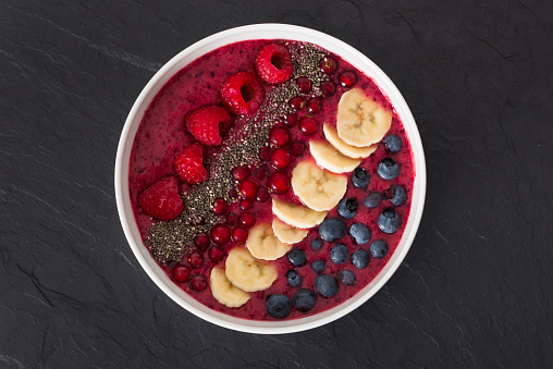 berry smoothie bowl with chia seeds, bananas, blueberries, currant and raspberries on black slate background