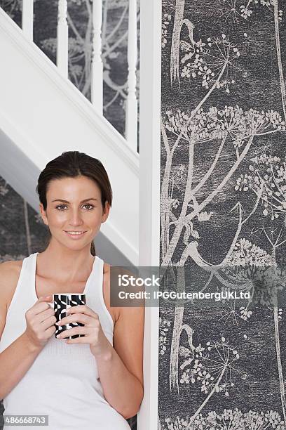 Beautiful Woman Holding Coffee Mug While Leaning On Door Frame Stock Photo - Download Image Now