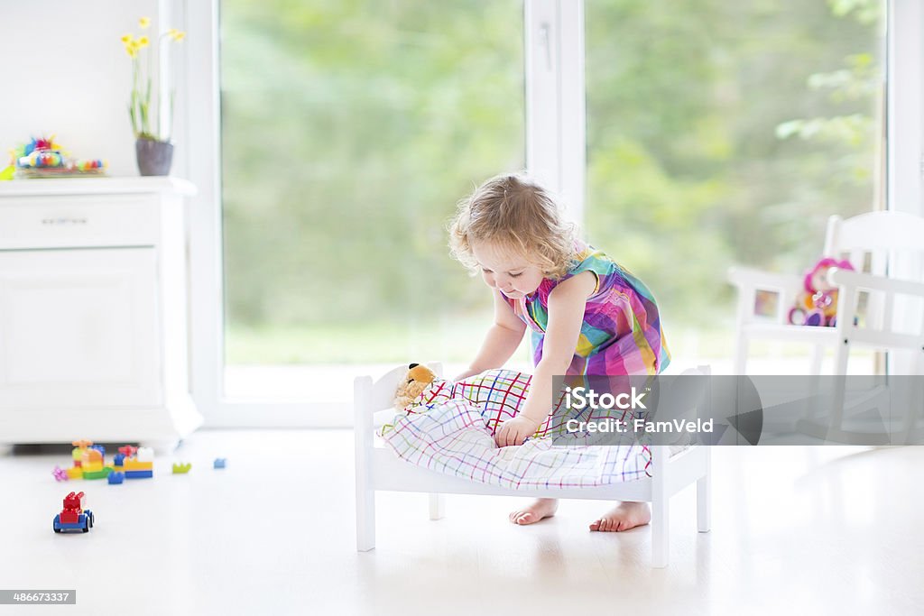 Cute curly toddler girl playing with bear in sunny room Cute curly toddler girl playing with her bear in a sunny room with big windows Baby - Human Age Stock Photo