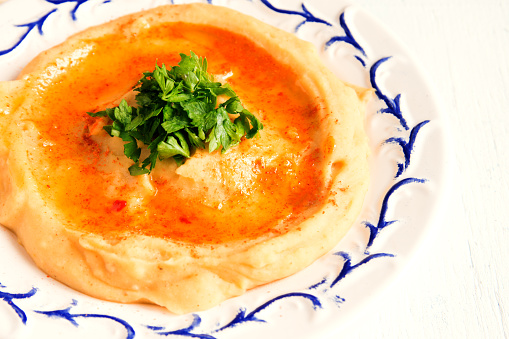 Hummus with parsley on plate and white wooden background close up